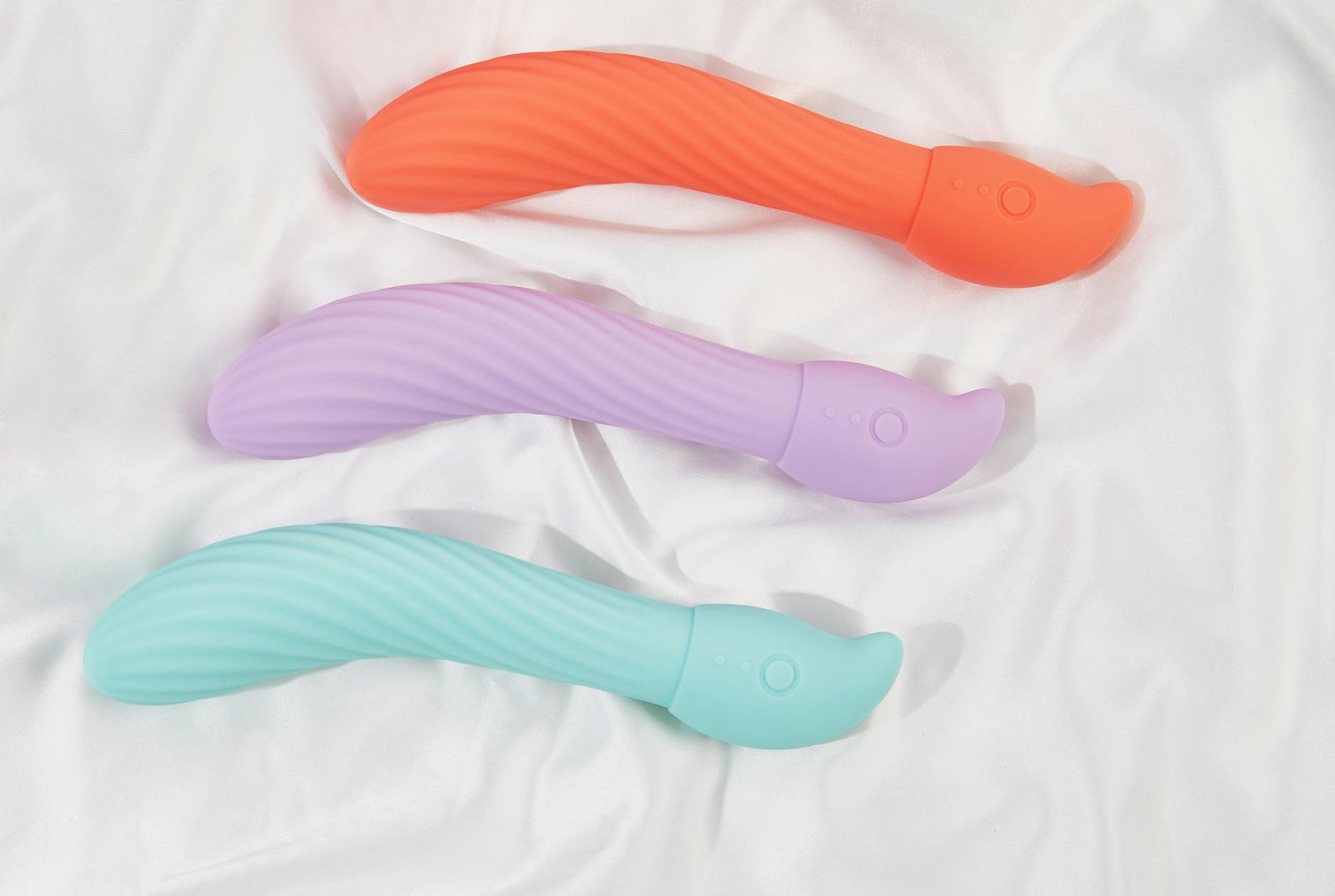 Three colorful vibrators arranged on white fabric, highlighting their smooth texture.