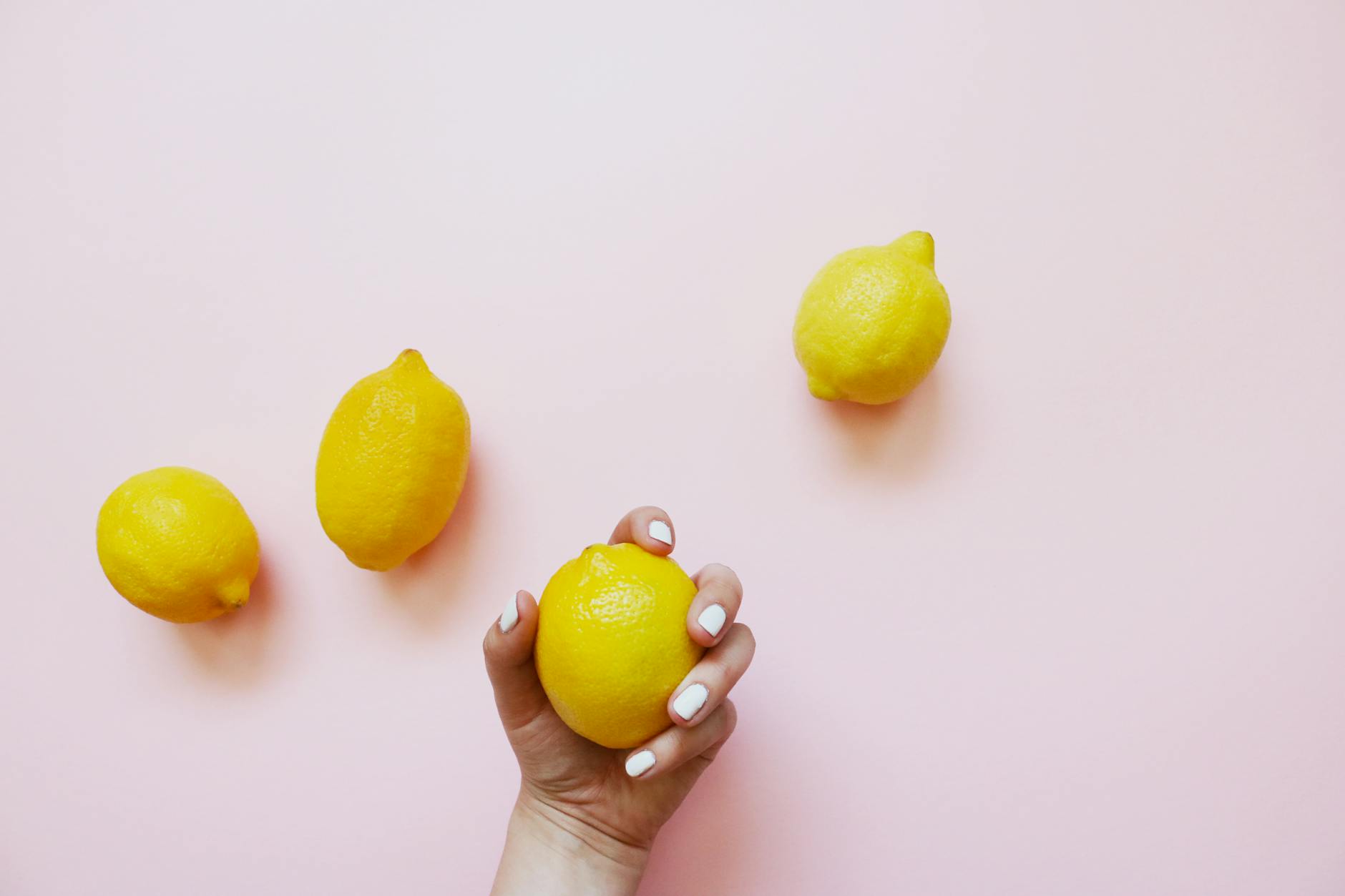 Hand holding a fresh lemon on a soft pink background