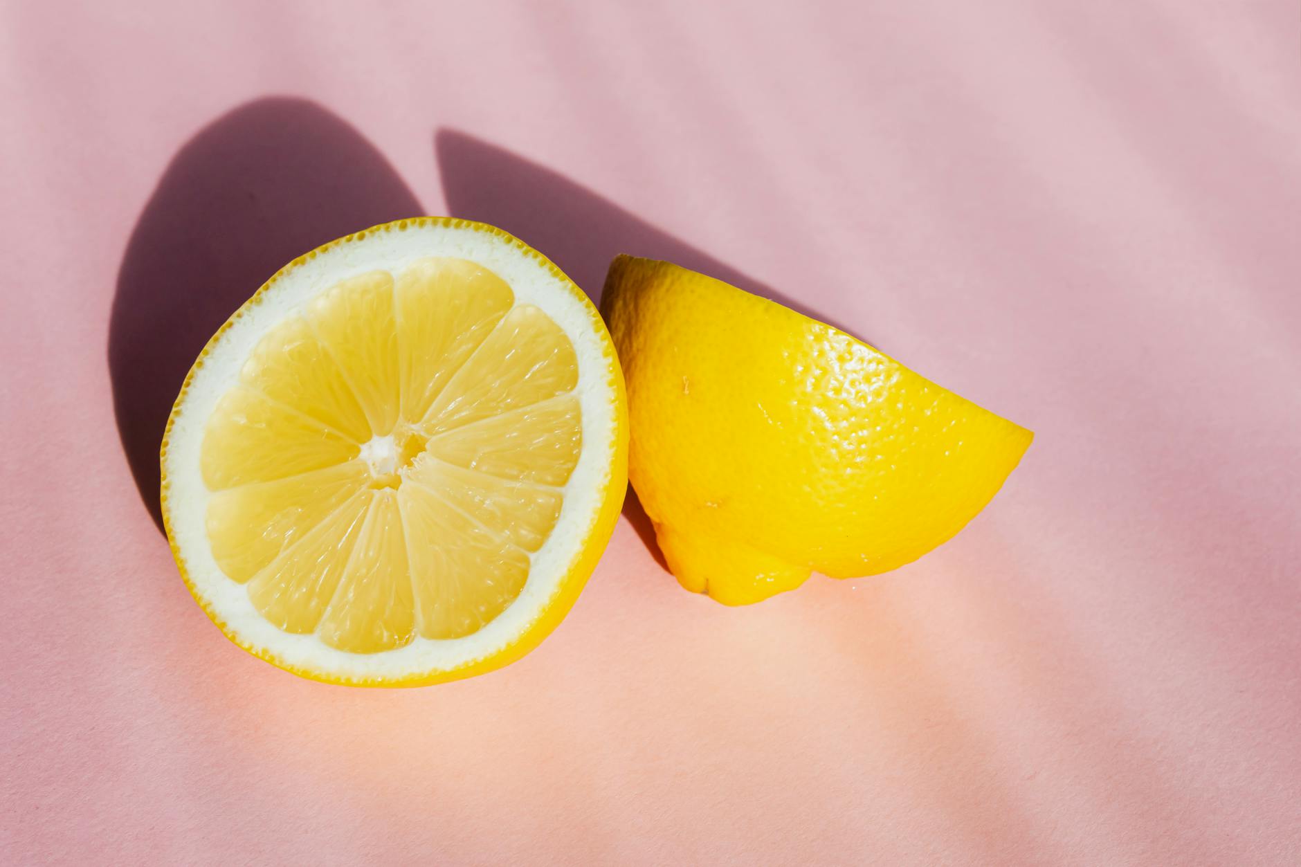 Fresh lemons halved and composed on a pink background in sunlight