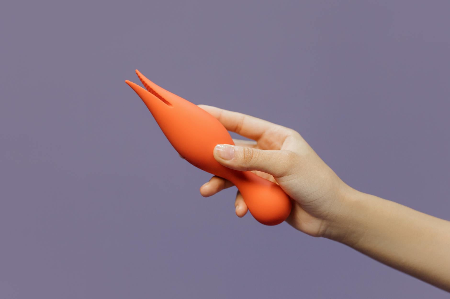 Hand holding a vibrant clitoral vibrator against a minimalist purple background, symbolizing modern pleasure and sensory control.