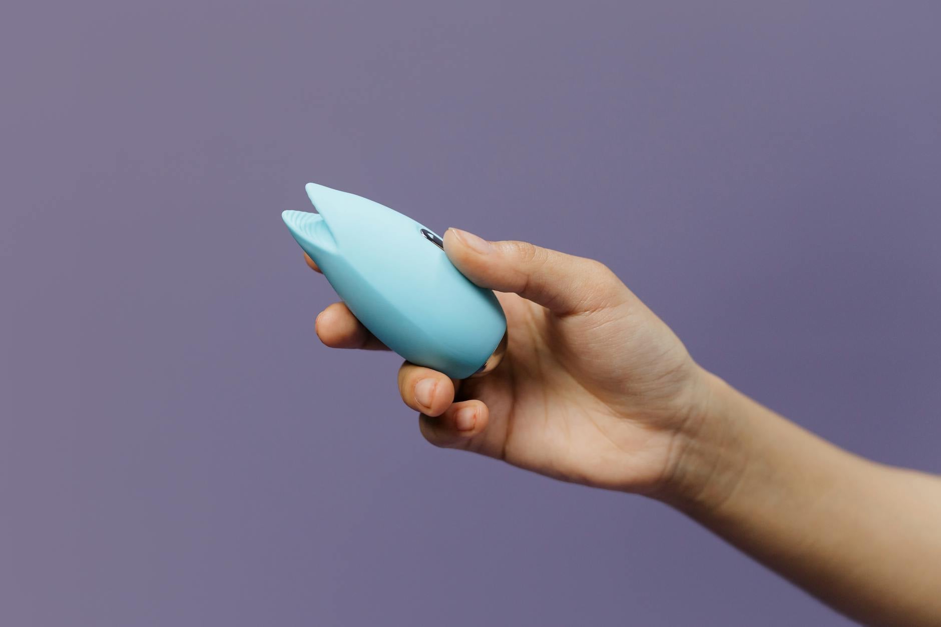 A blue silicone vibrator held against a purple background, showing the Lem design for clitoral stimulation.