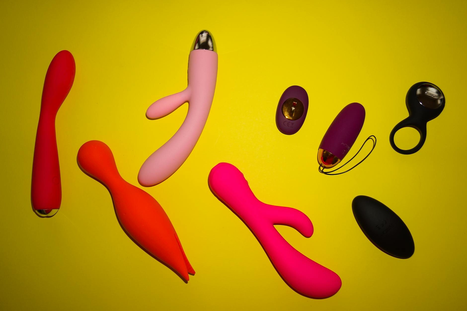 Vibrant collection of colorful clitoral vibrators arranged on a bright yellow surface